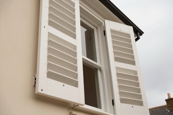 White plantation shutters partially open on a sash window.