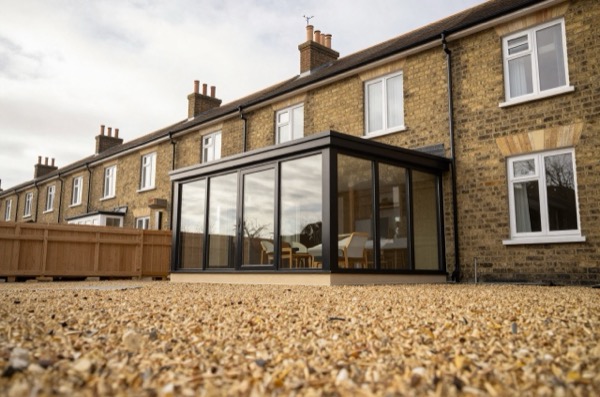 Black-framed glass box extension on a brick terrace.