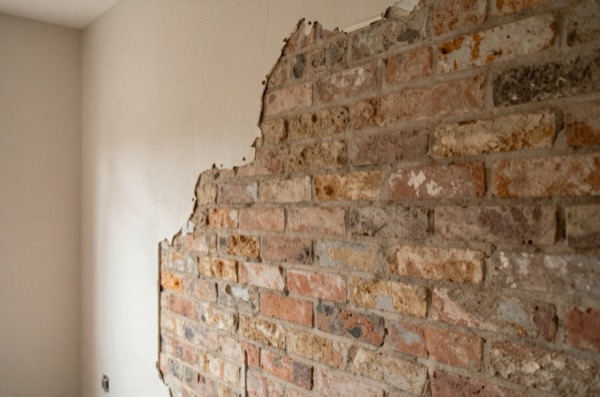 Exposed solid brickwork next to plasterboard partition.