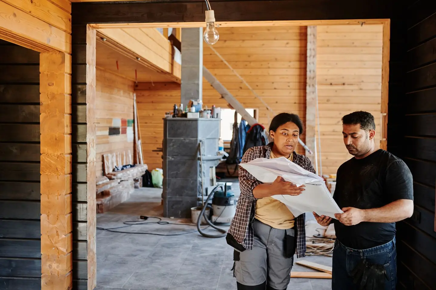 Construction workers reviewing blueprints indoors at a renovation site with wooden walls.