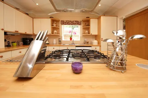 A bright and modern kitchen interior featuring a gas hob, knife block, and cutlery holder on a wooden worktop.