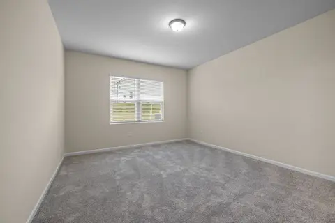 Bright and empty room with carpet flooring and large window, perfect for home staging.