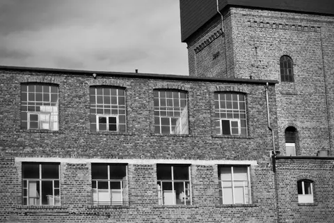 Black and white photo of a historic red brick industrial building with large windows.