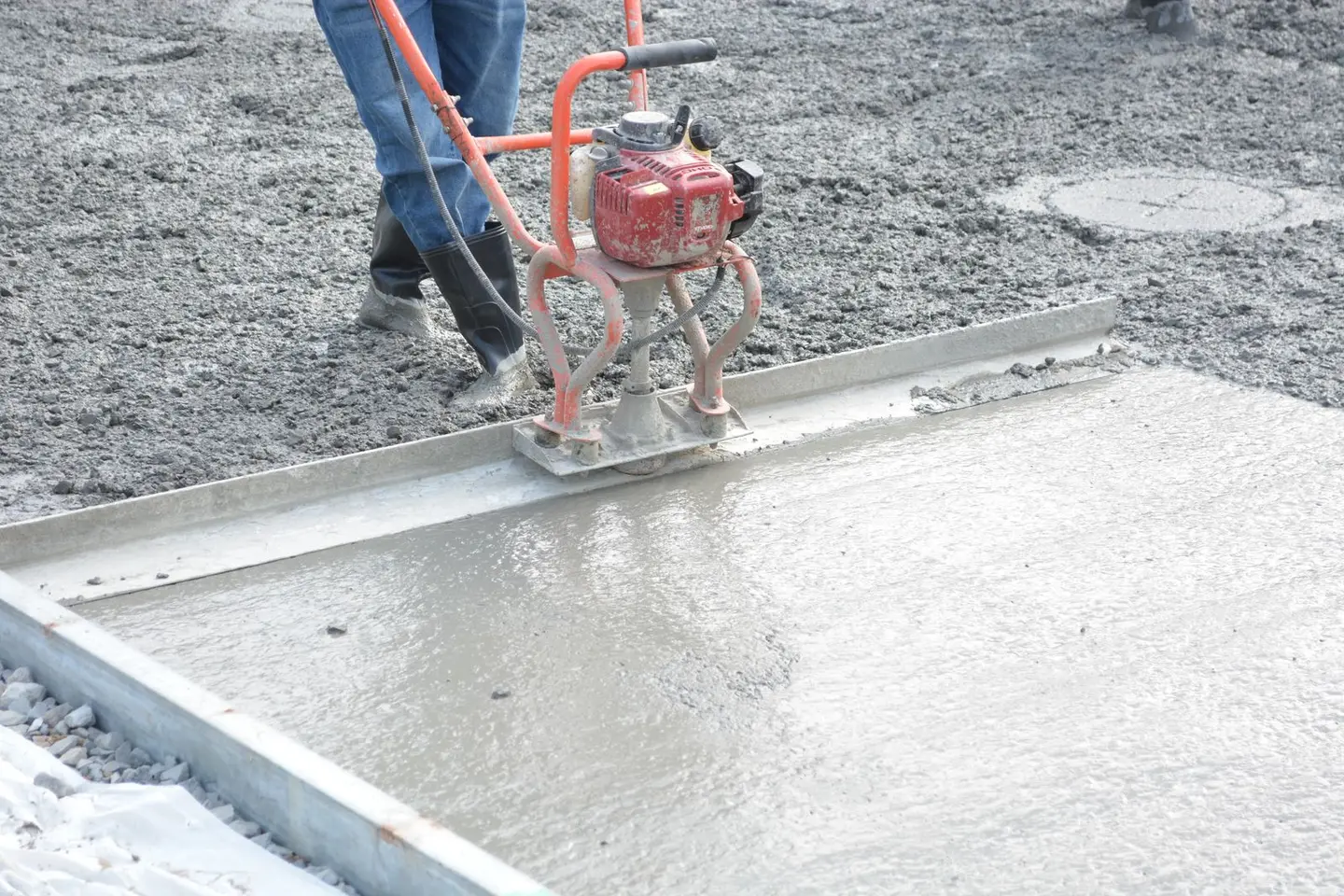 A construction worker operates a power trowel to smooth freshly poured concrete on a construction site.