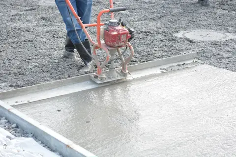 A construction worker operates a power trowel to smooth freshly poured concrete on a construction site.