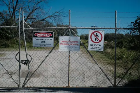 Metal gate with warning signs at a construction site prohibiting entry and dumping.