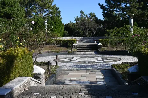A serene stone pathway leads to a garden surrounded by lush greenery and geometric paving design.