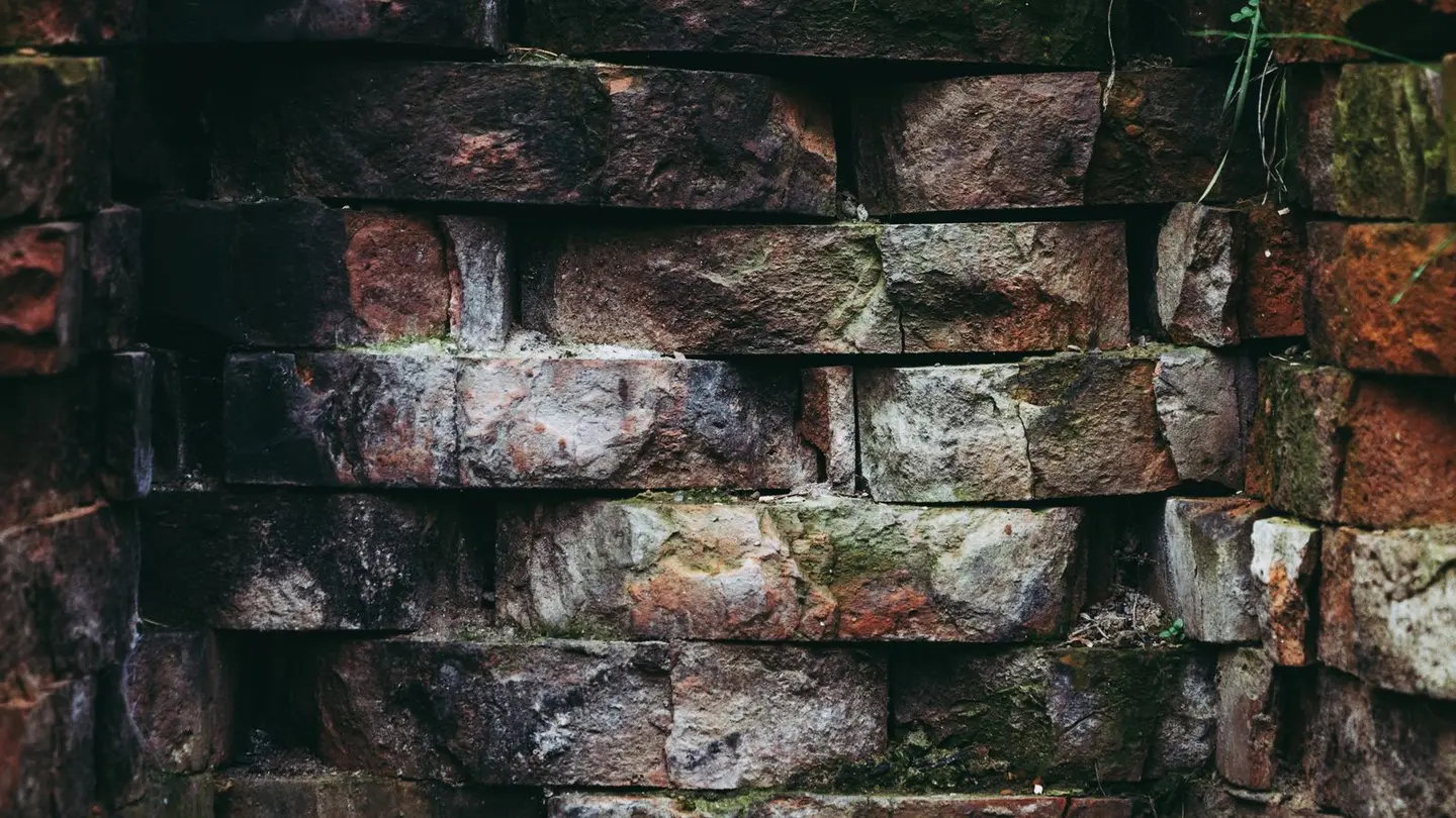 Close-up of a rustic, moss-covered brick wall showcasing weathered textures and patterns.