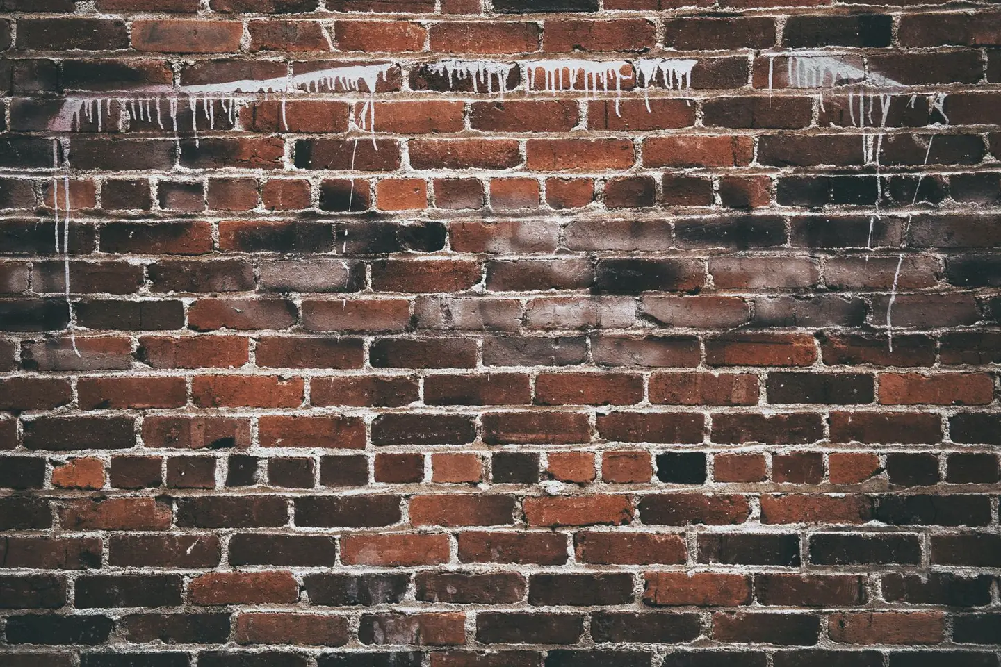 A close-up of a red brick wall with white paint drippings, offering a textured urban background.