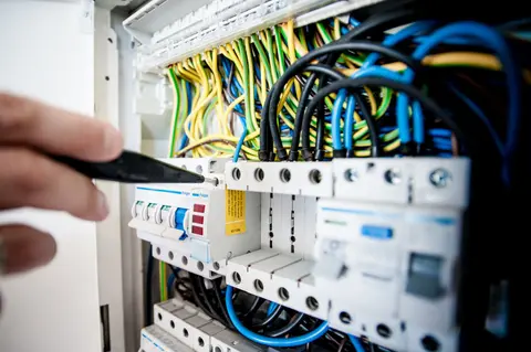 Hand of electrician working on a circuit breaker panel with colourful wires, ensuring safe electrical connections.
