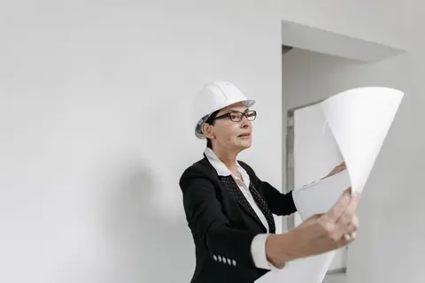 A professional female architect in a hard hat examines building plans on a construction site.