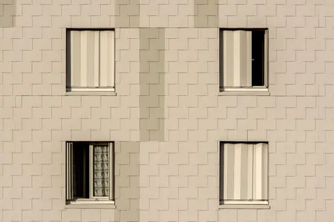Close-up of a modern apartment building facade with symmetrical windows and beige cladding.