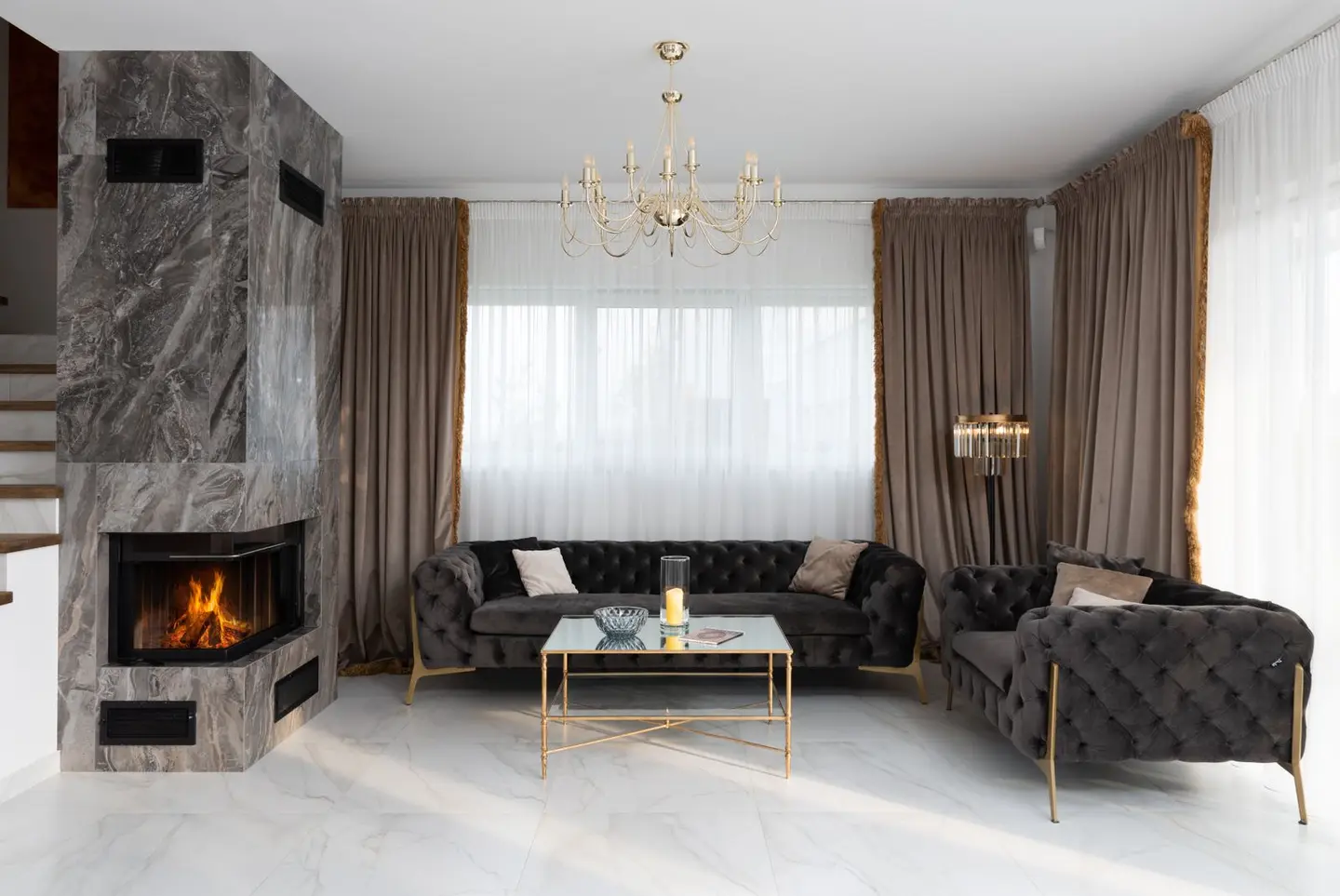 Interior of modern living room with soft couches and side table placed near windows with curtains and burning fireplace at home