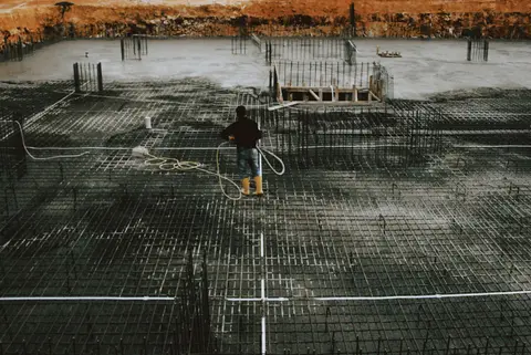 A worker stands on a reinforced concrete foundation, preparing for construction.
