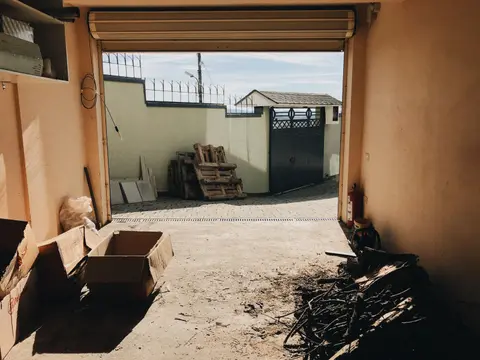 View from inside a garage showing open roller shutter, cardboard boxes, and an outdoor concrete fence.