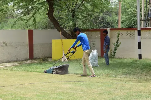 Young men working together on lawn maintenance with a mower in a sunny garden setting.