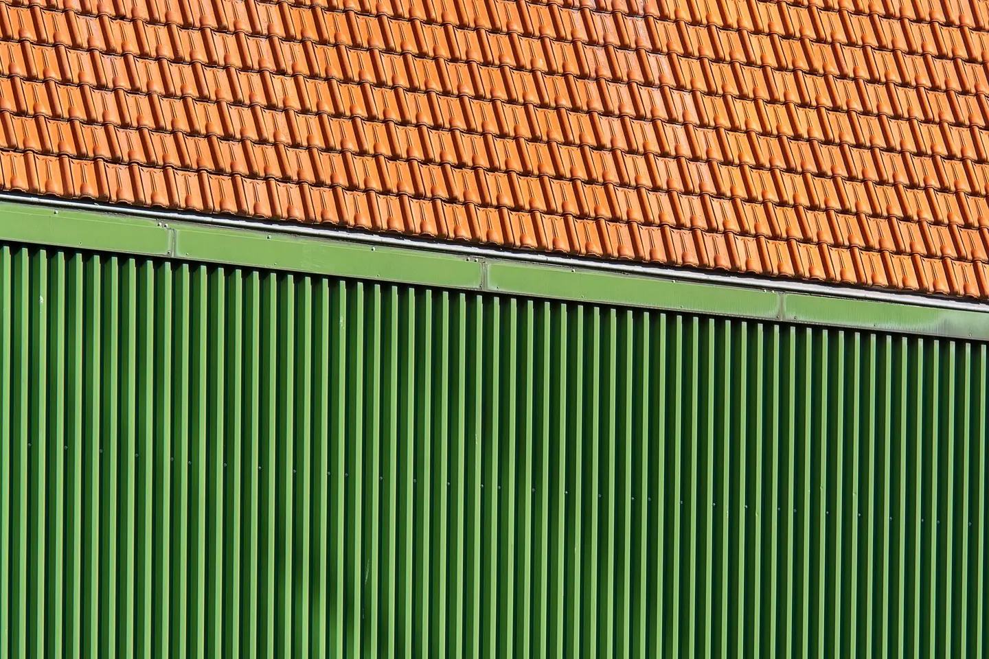 Close-up of vibrant orange roof tiles and green corrugated wall.