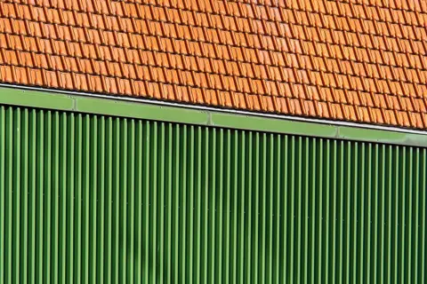 Close-up of vibrant orange roof tiles and green corrugated wall.