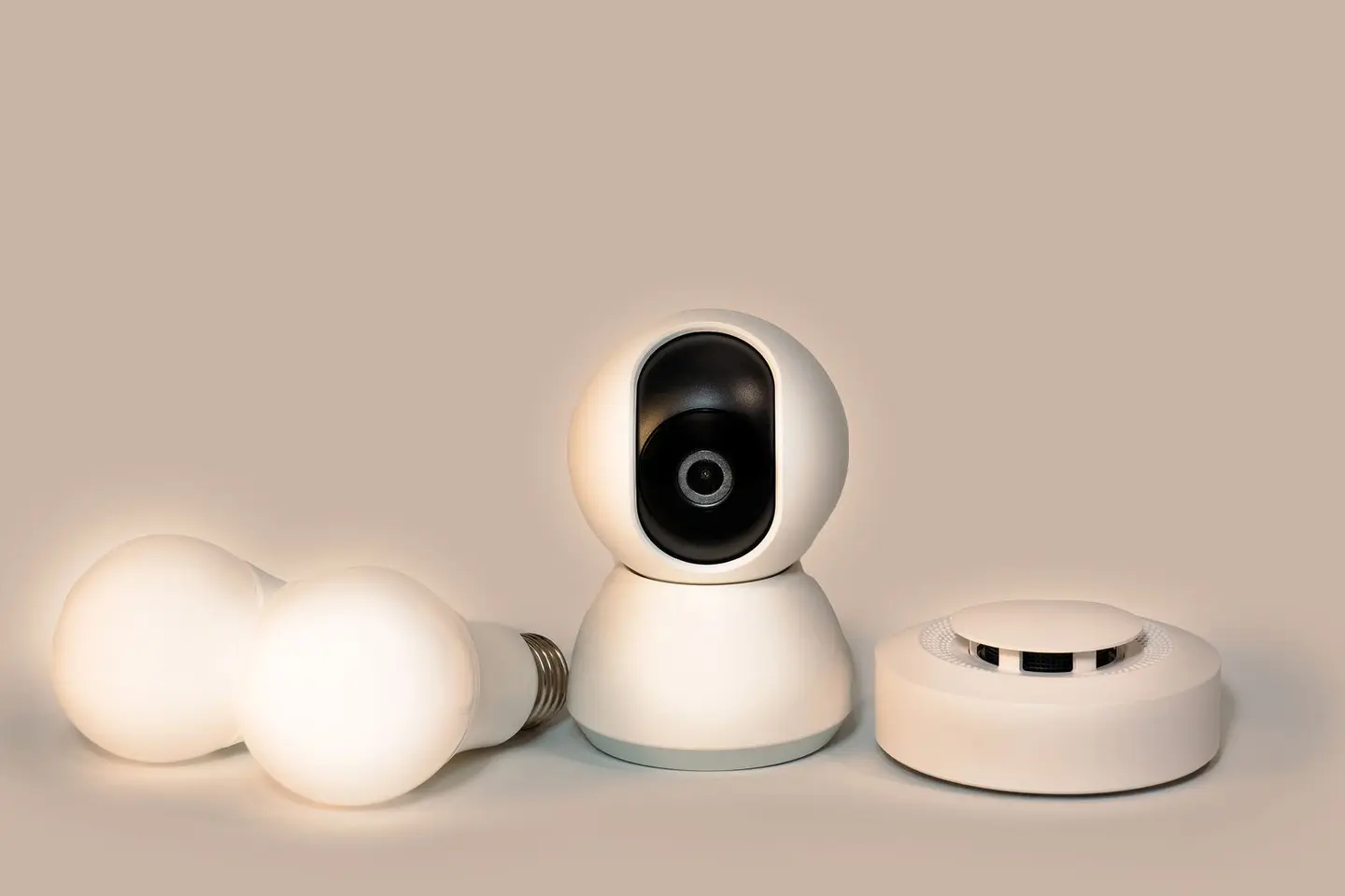 A collection of modern smart home gadgets including a CCTV camera, LED bulbs, and a smoke detector.