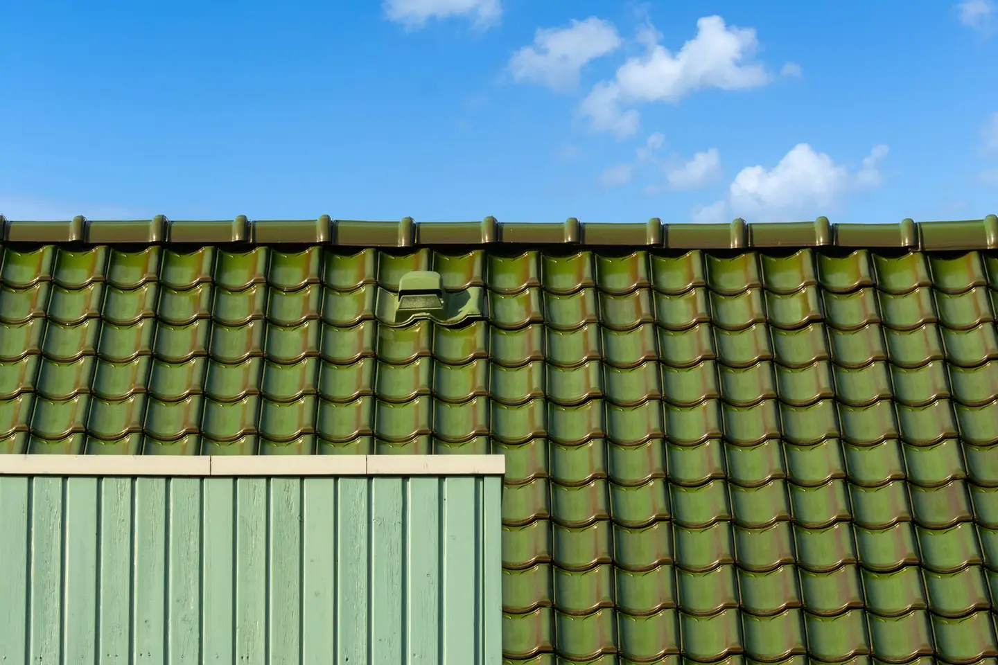 Closeup of a green tiled roof under a bright blue sky, capturing architectural detail and colour contrast.
