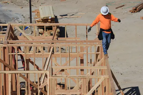 Construction worker balances carefully on a wooden frame at a building site, emphasizing safety and skill.