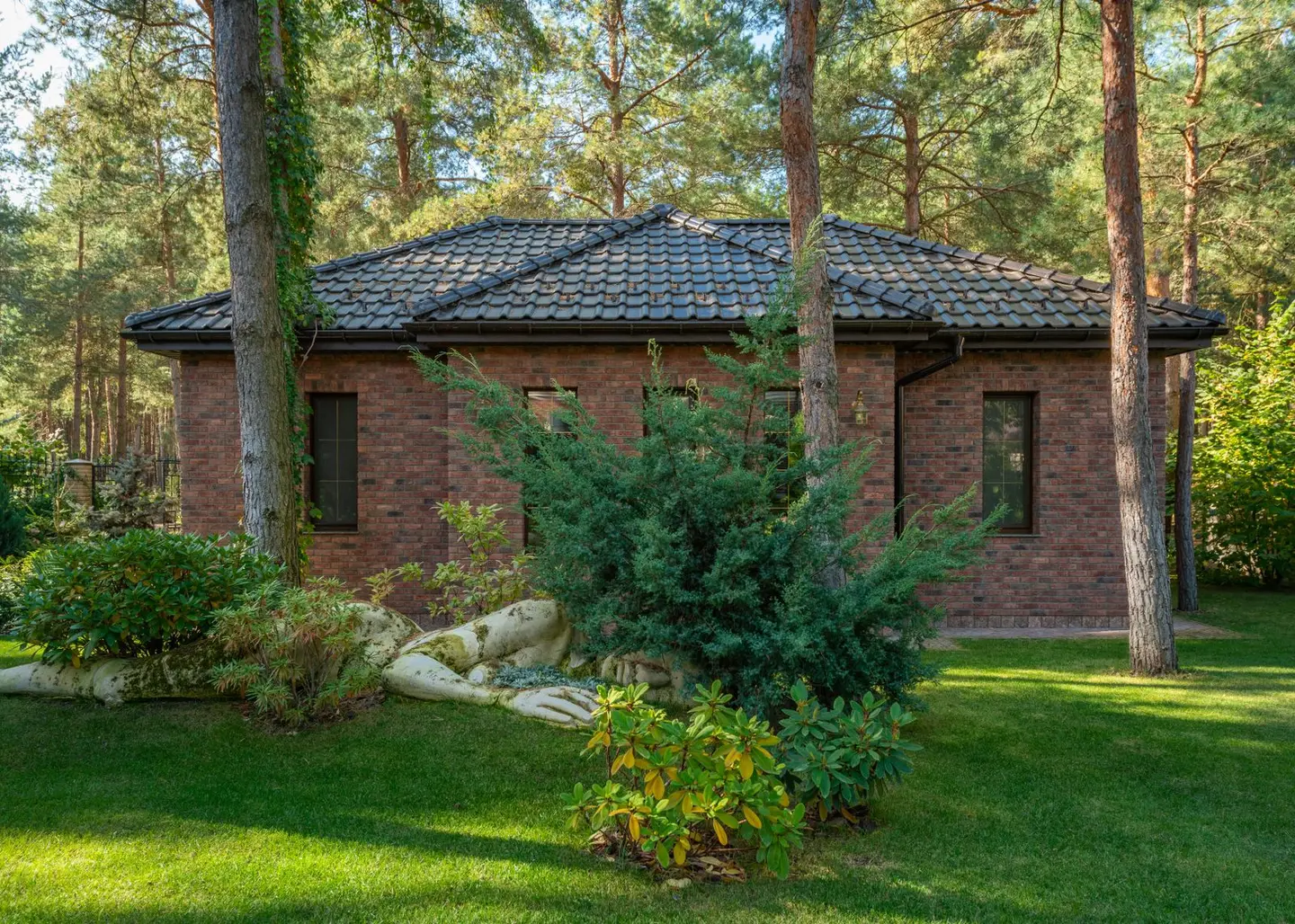 A modern brick house surrounded by a lush forest and lawn, featuring serene outdoor landscaping.