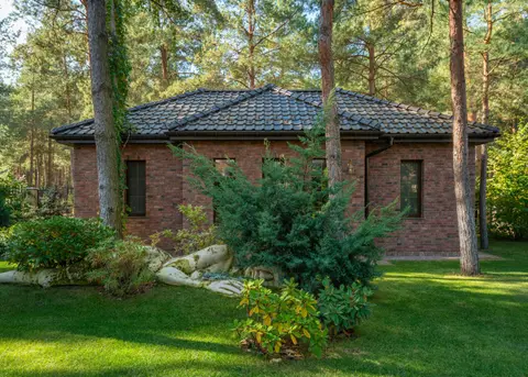 A modern brick house surrounded by a lush forest and lawn, featuring serene outdoor landscaping.
