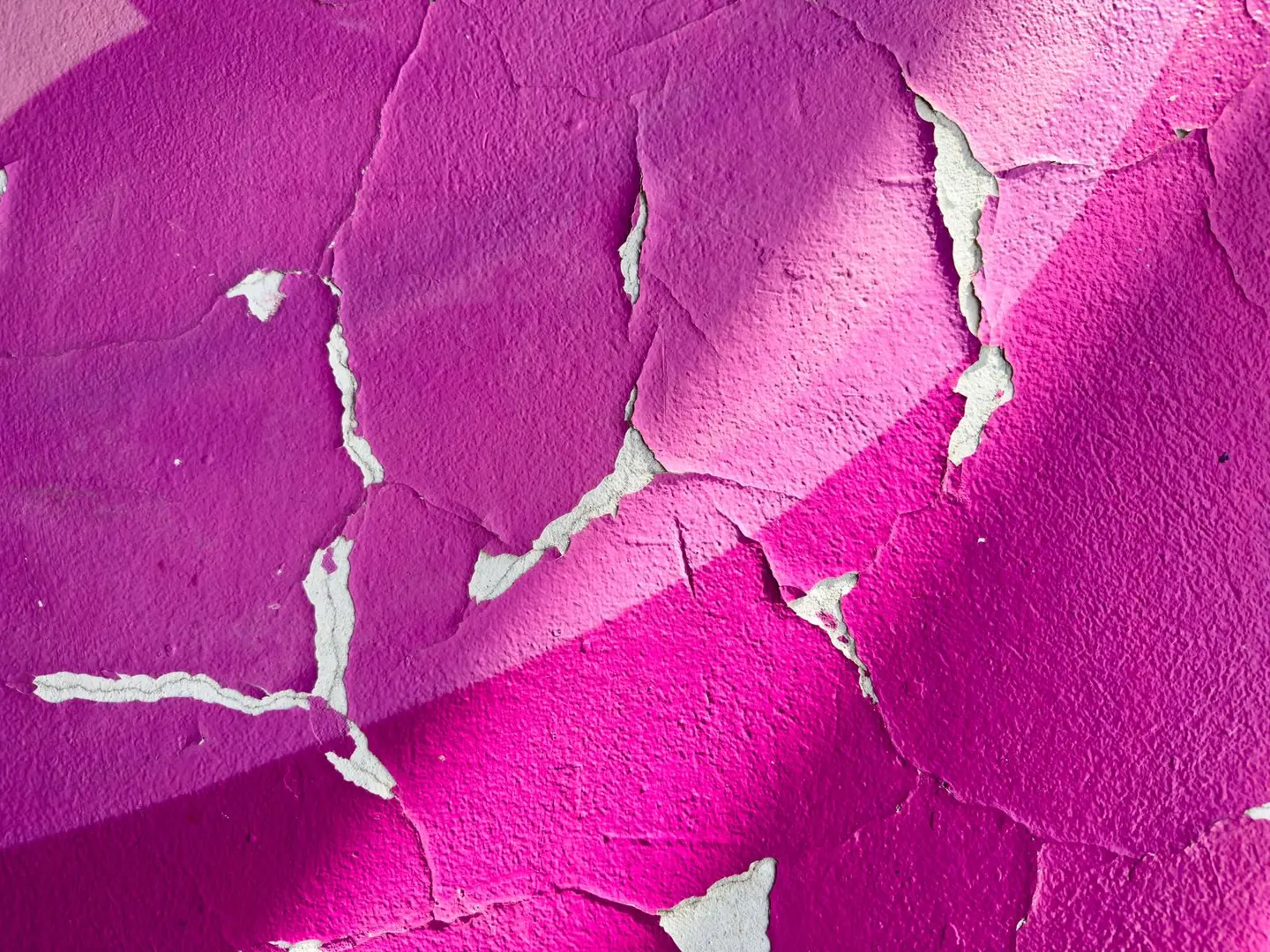 Close-up of cracked purple paint on a wall, featuring textured surface patterns.