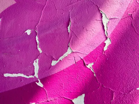 Close-up of cracked purple paint on a wall, featuring textured surface patterns.
