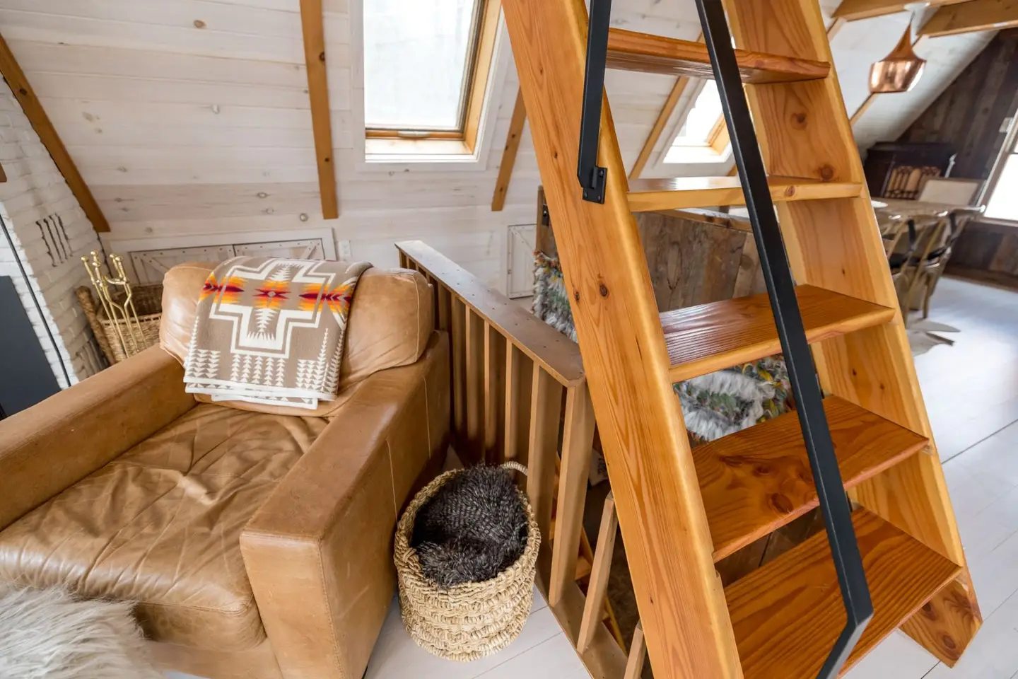 Explore the warmth and charm of a modern A-frame cabin loft with wooden ladder and cozy seating area.