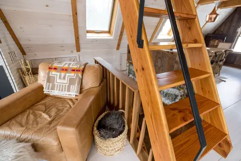 Explore the warmth and charm of a modern A-frame cabin loft with wooden ladder and cozy seating area.