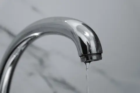 A close-up shot of a modern chrome bathroom tap with water dripping from the tip.