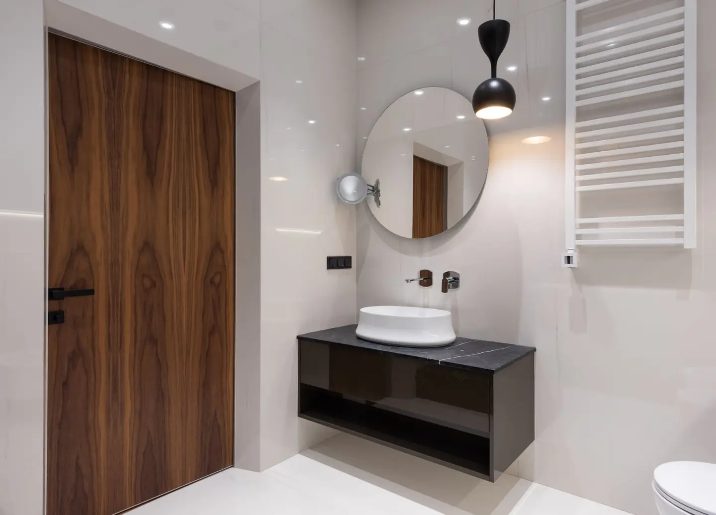 Interior of modern bright bathroom with sink on counter under round mirror near toilet and lamp hanging from ceiling nea