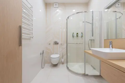 Shower cabin with transparent glass doors near toilet bowl and sink in modern bathroom with wooden furniture and tiled walls