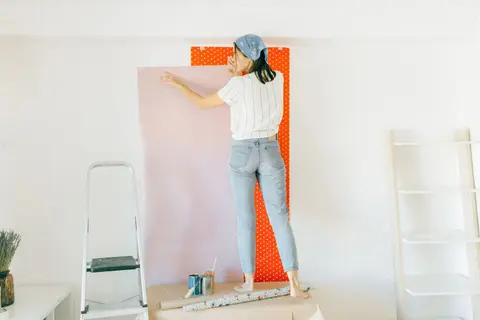 A woman applying wallpaper on a wall for home renovation indoors.