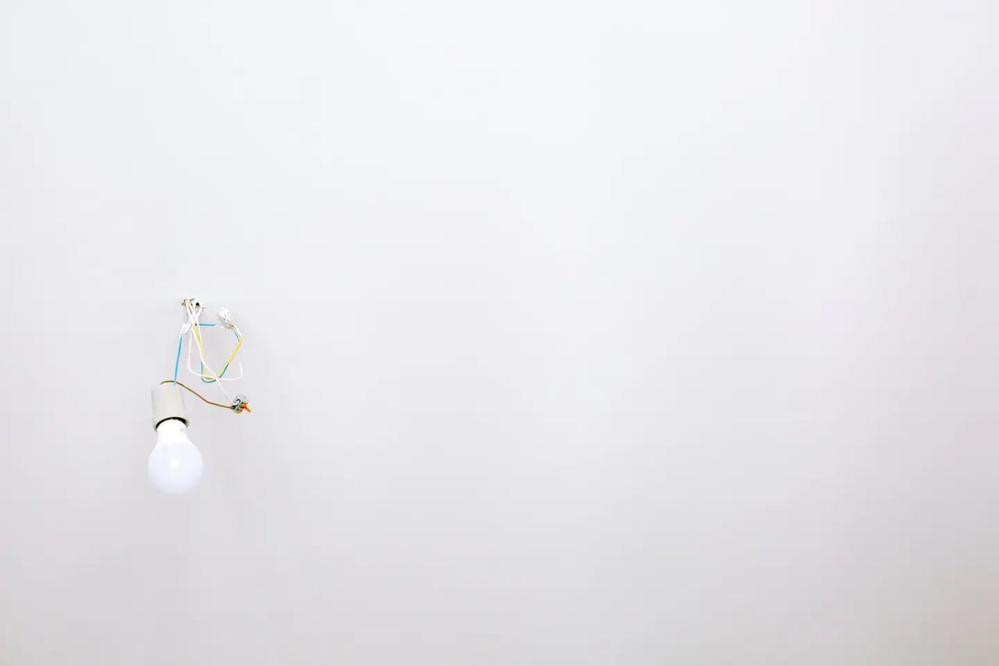 A minimalist light bulb with exposed wires hanging from a white ceiling, ideal for home renovation themes.