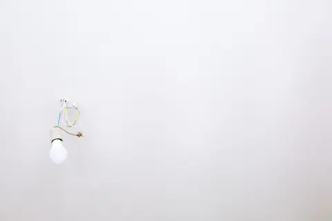 A minimalist light bulb with exposed wires hanging from a white ceiling, ideal for home renovation themes.