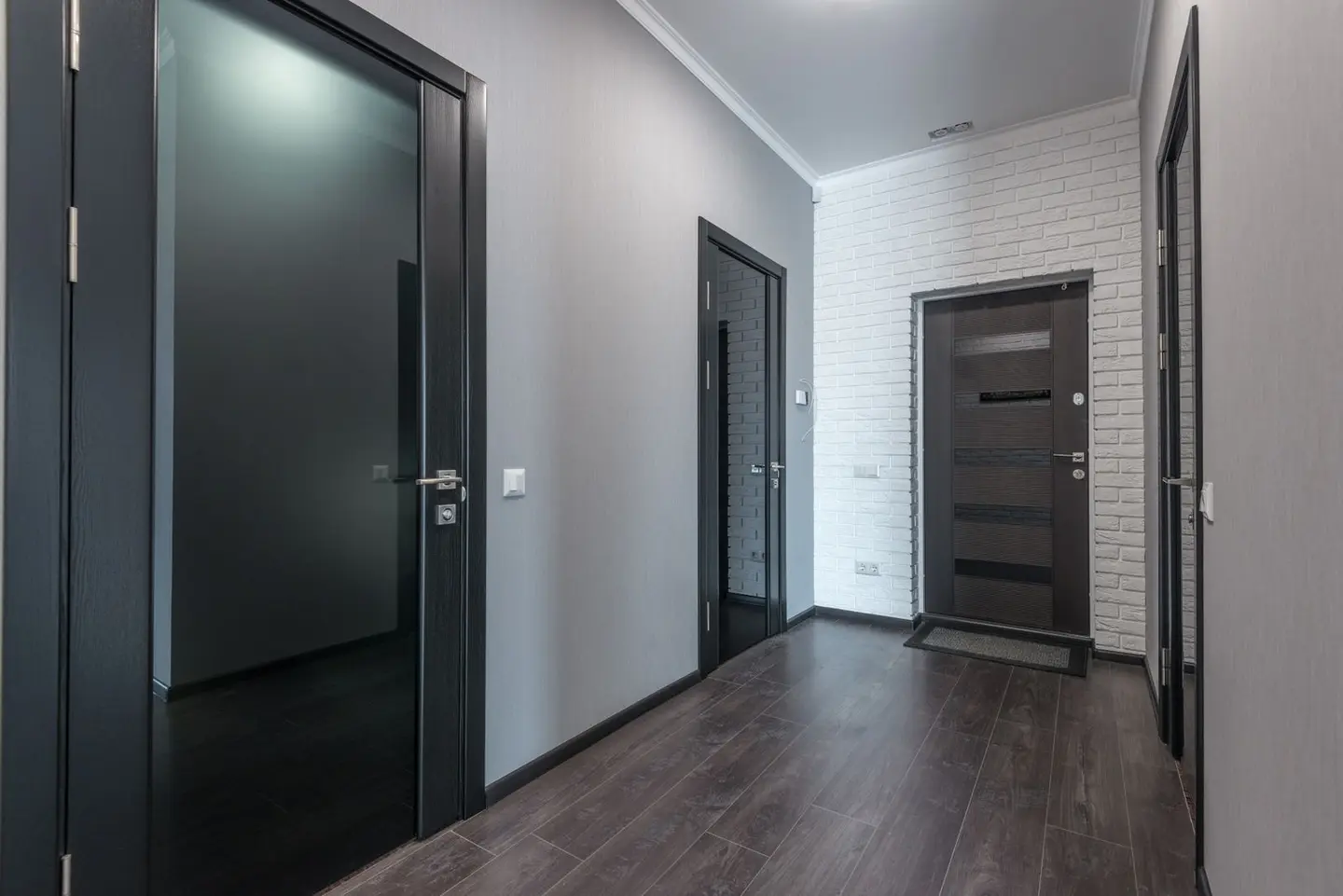 Interior of empty spacious corridor with laminate floor and black doors with glass parts and white ceiling and grey pain