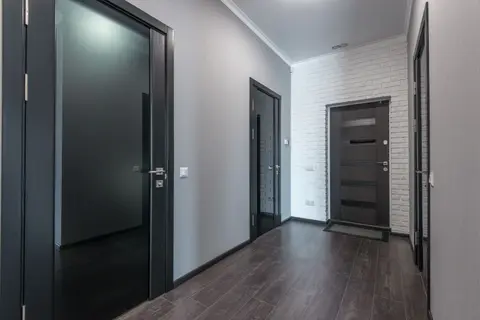 Interior of empty spacious corridor with laminate floor and black doors with glass parts and white ceiling and grey pain