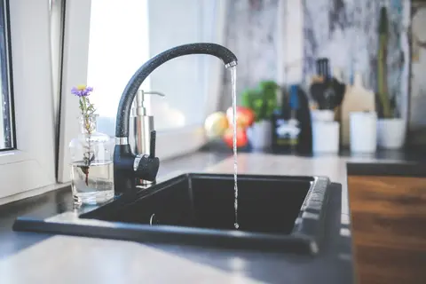 A modern kitchen sink with running water, a sleek tap, and a vase on the worktop.