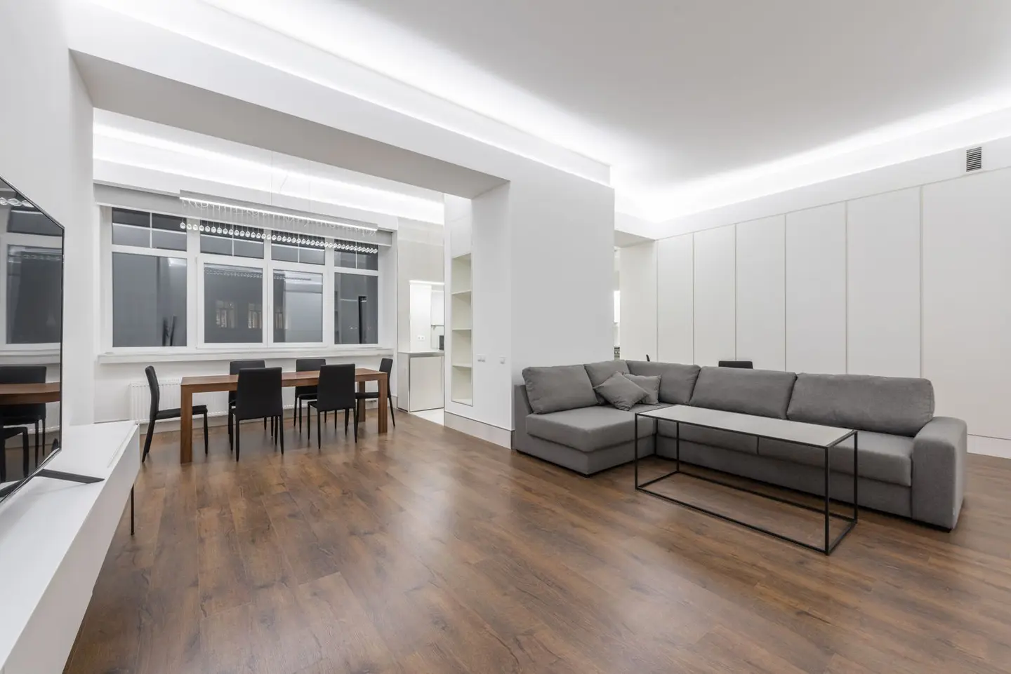 Comfortable couch placed against TV near wooden table with chairs in modern apartment with minimalist interior and parti