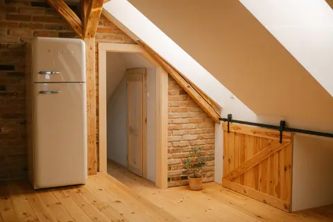 Rustic attic loft with wooden beams, vintage fridge, and warm ambiance.