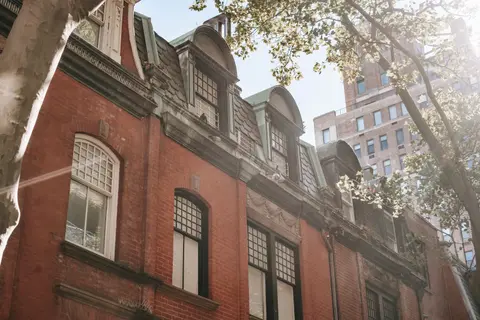 From below of tree growing near stylish aged brick building with mansard windows located on city residential district on