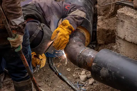 Close-up of a skilled worker welding a steel pipe outdoors at a construction site.