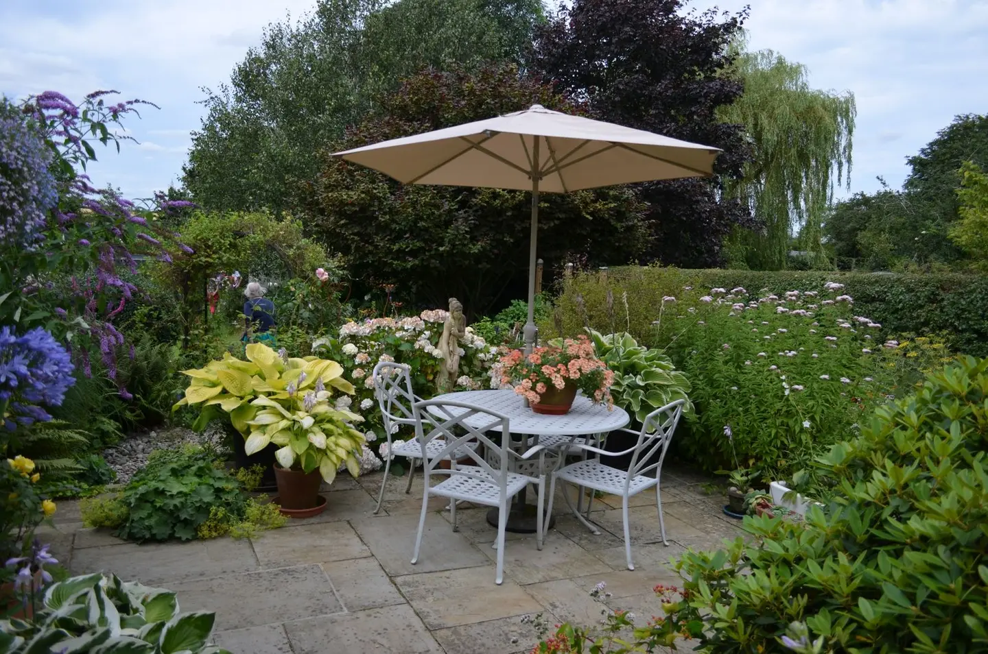 A serene garden patio featuring a table with chairs, umbrella, and vibrant flowers in full bloom.
