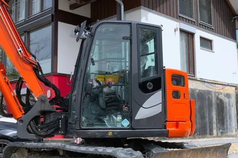 Side view of a construction excavator parked near a Swiss chalet, showcasing modern building equipment.