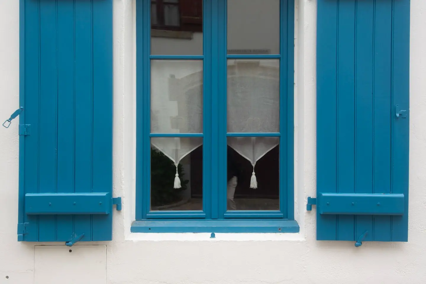Close-up of blue shutters and window on a rustic white wall, showcasing classic architecture.
