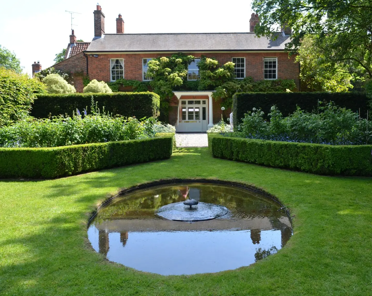 Serene garden with fountain in front of a classic brick house on a sunny day.