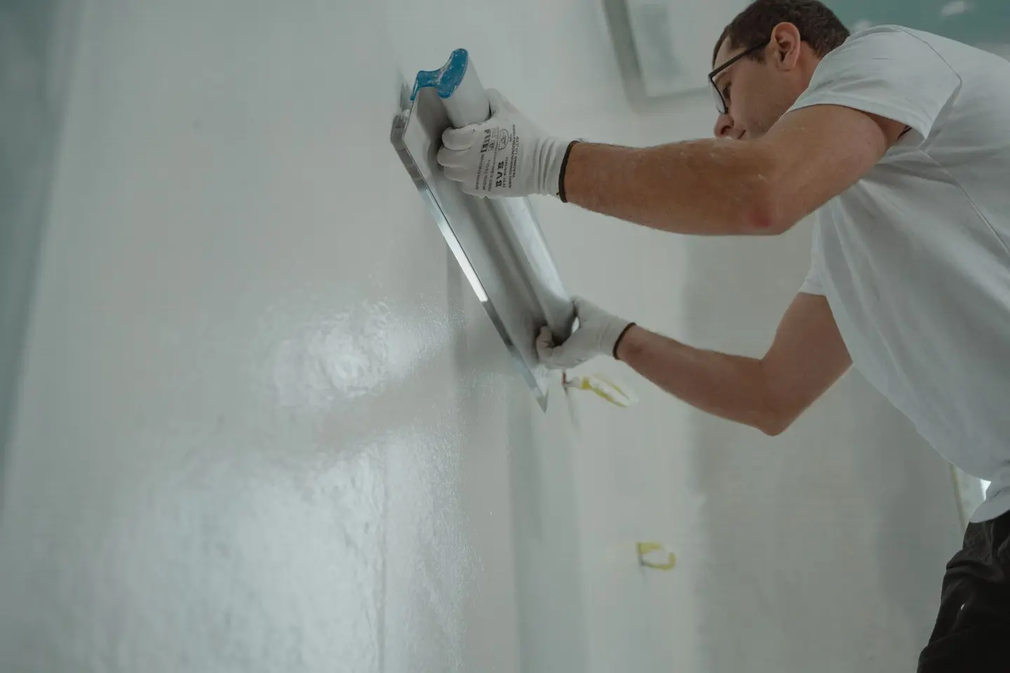 A man works on home renovation, applying plaster to an interior wall for a smooth finish.