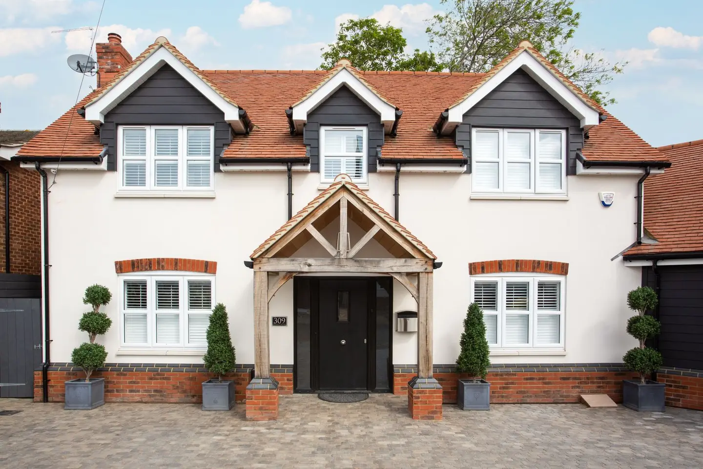 An oak framed open porch added to the front door of a rendered British house with a clay tiled roof.
